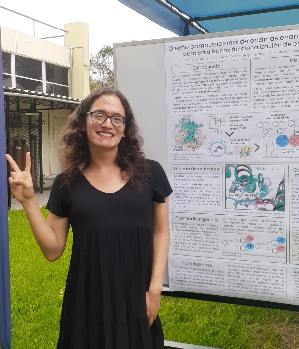 A photo of Adelaide in a black dress, standing outside in a garden, in front of a scientific poster about artificial enzymes. She has curly hair, wears square glasses and is doing a peace sign and smiling at the camera. The sky is cloudy behind her.